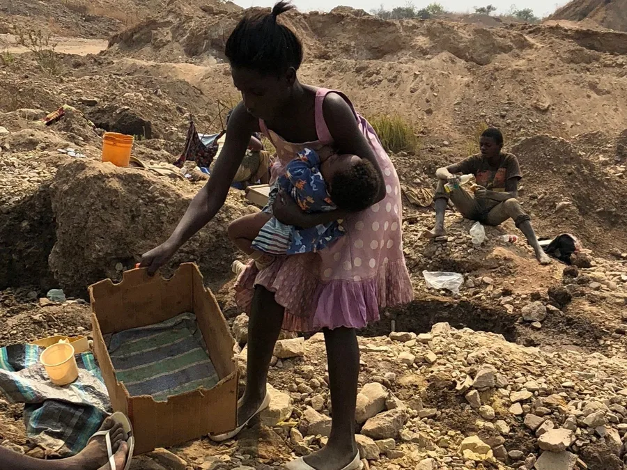 Woman holding a child while working at an artisanal cobalt mining site
