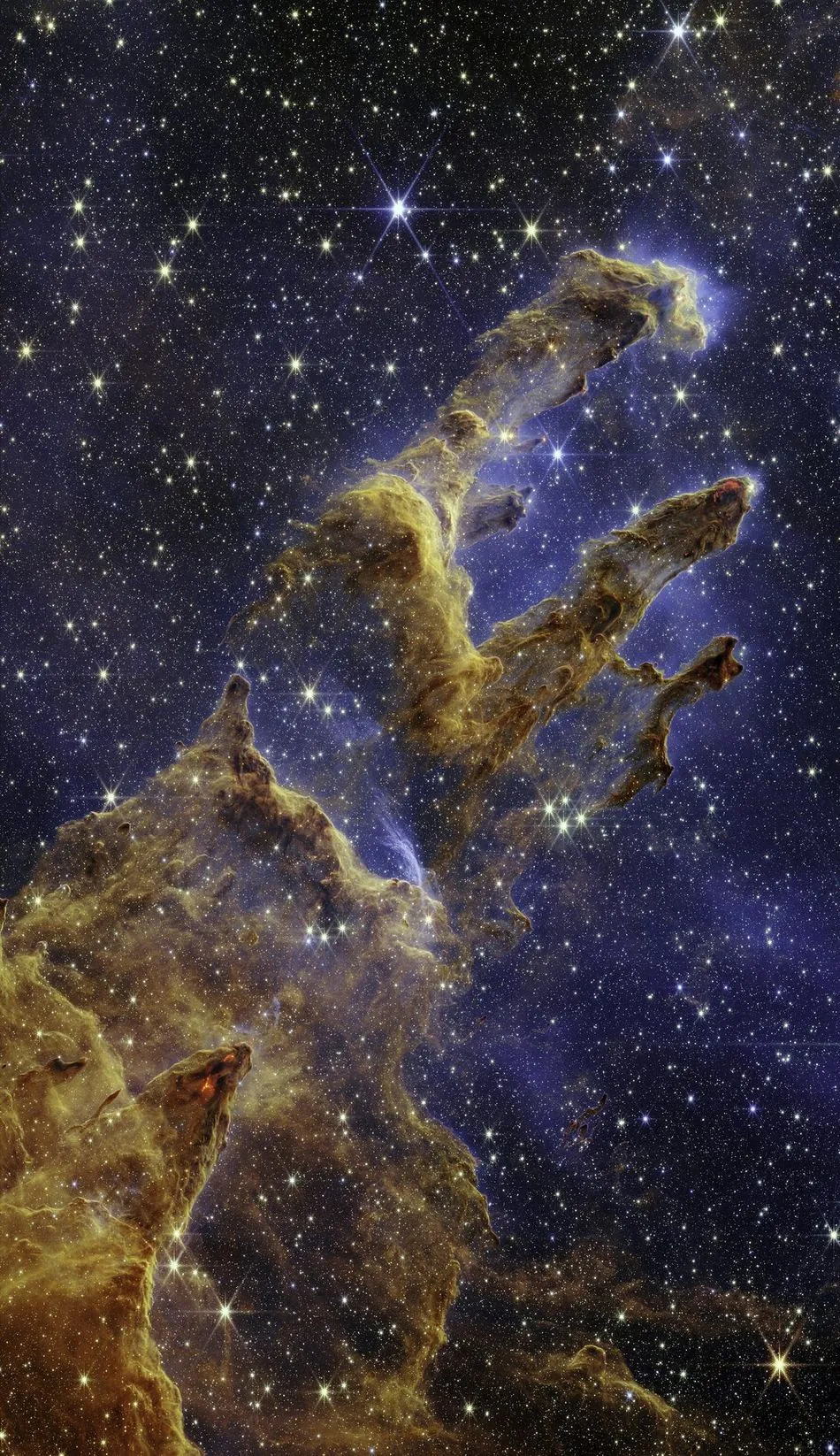 The Pillars of Creation photographed by the James Webb Space Telescope: towering columns of brown and orange interstellar gas and dust studded with newly formed stars