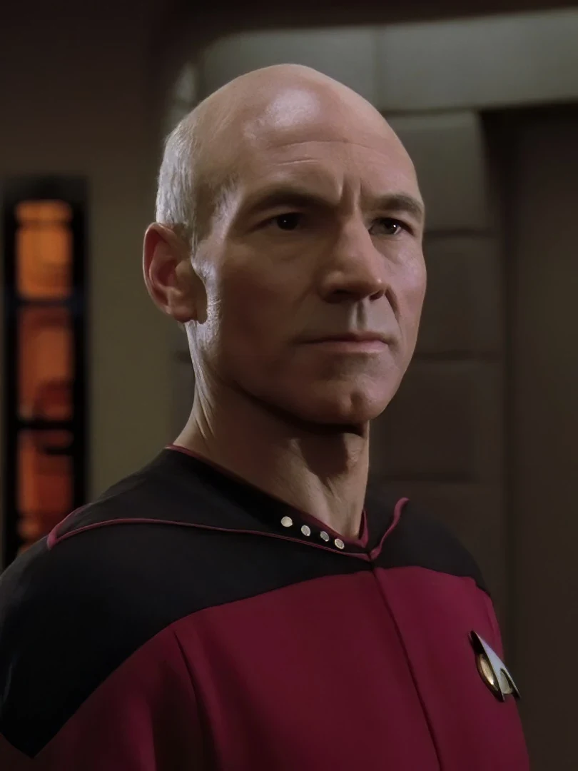 Sir Patrick Stewart as Captain Jean-Luc Picard in his red and black Starfleet uniform, with four rank pips on his collar and a combadge on his chest, looking steadily off to one side