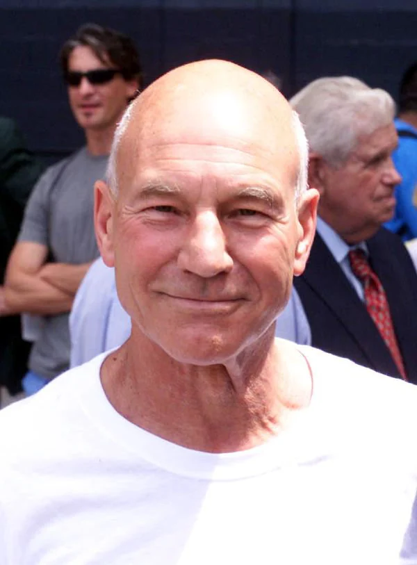 Sir Patrick Stewart in a white T-shirt, smiling in a crowd of spectators