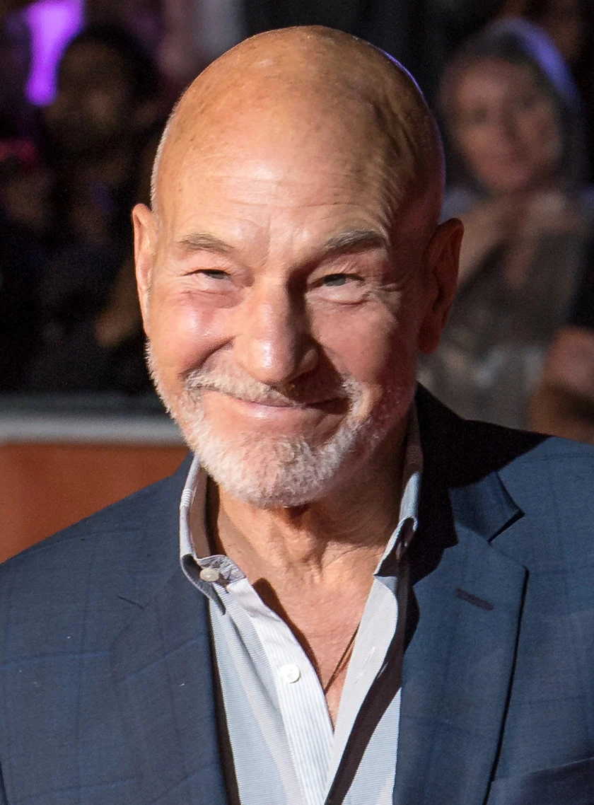 Sir Patrick Stewart in a dark jacket and open-necked shirt, smiling at a film premiere