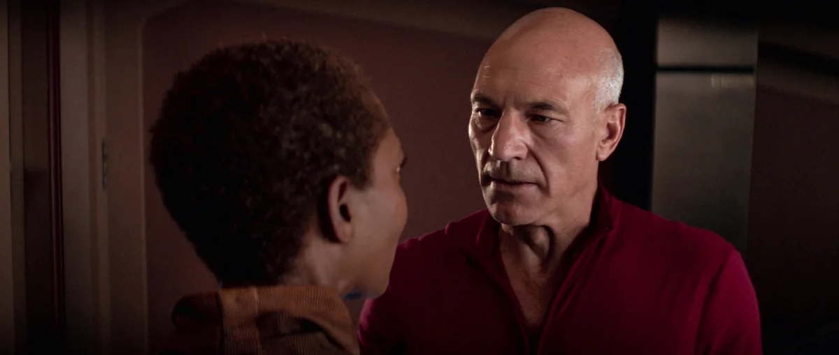 Lily Sloane, seen from behind, face to face with Picard in the dim observation lounge