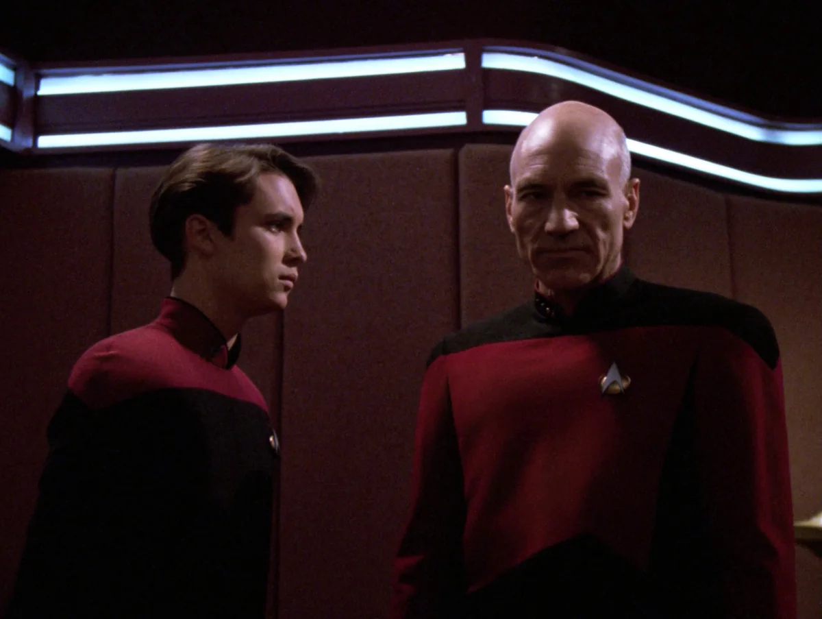 Picard and Wesley Crusher, in a red cadet uniform, standing facing each other
