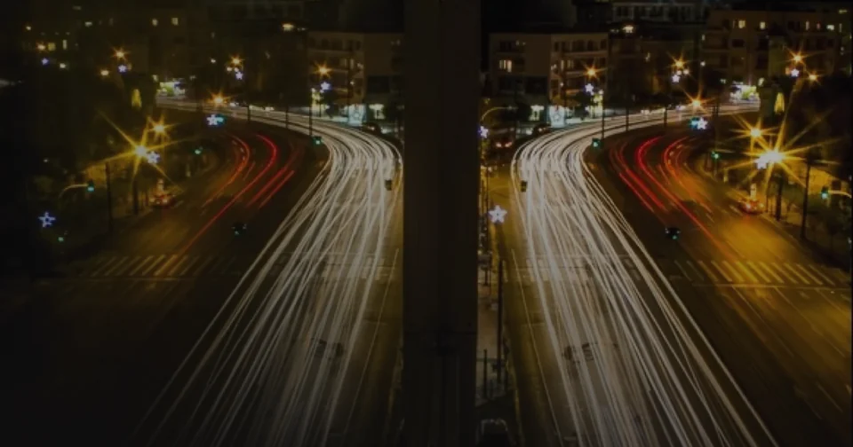 A night photo of light trails on a road, darkened towards the bottom and the left