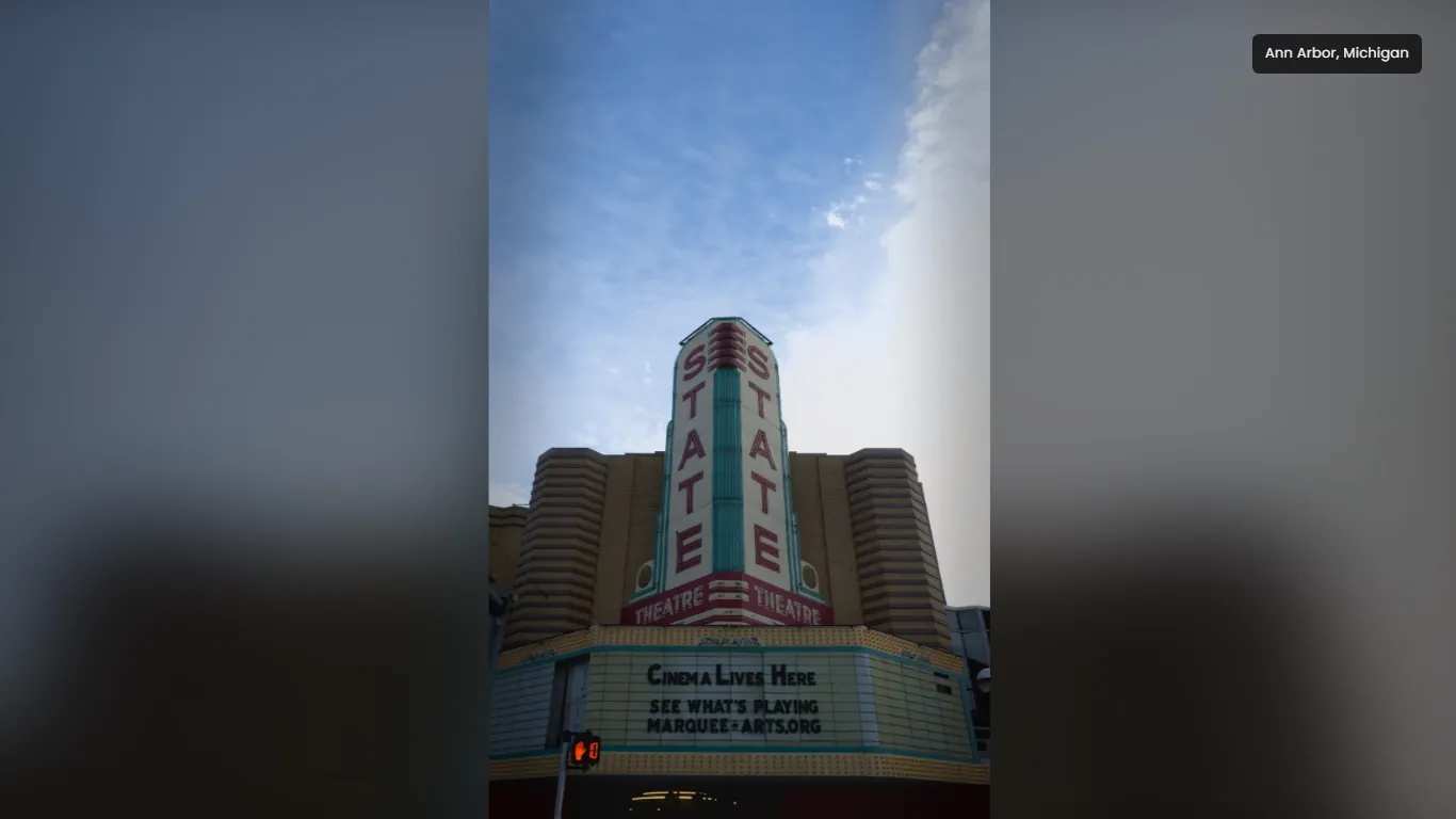 A tall photograph of the State Theatre's vertical sign and marquee in Ann Arbor, shown whole in the middle of a wide screen, with a blurred copy of the same photograph filling the space either side