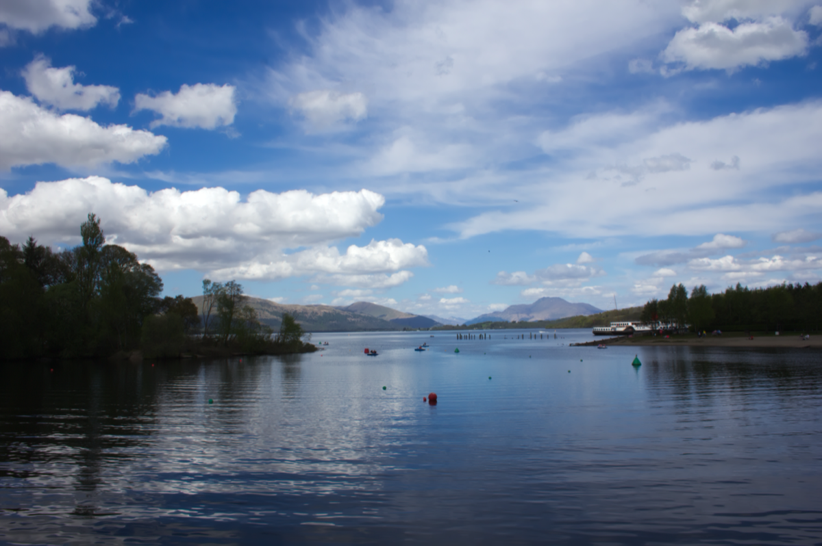 A still loch surrounded by mountains under a moody sky
