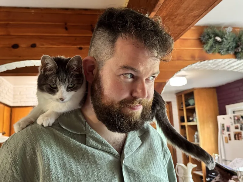Ken with a grey and white cat perched on his shoulder