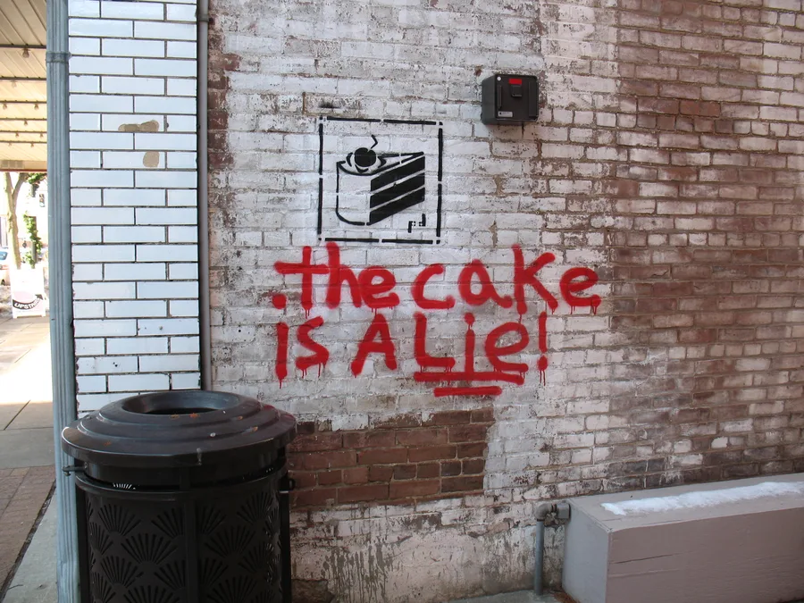 Graffiti reading 'The cake is a lie' on a dark wall, referencing the Portal video game