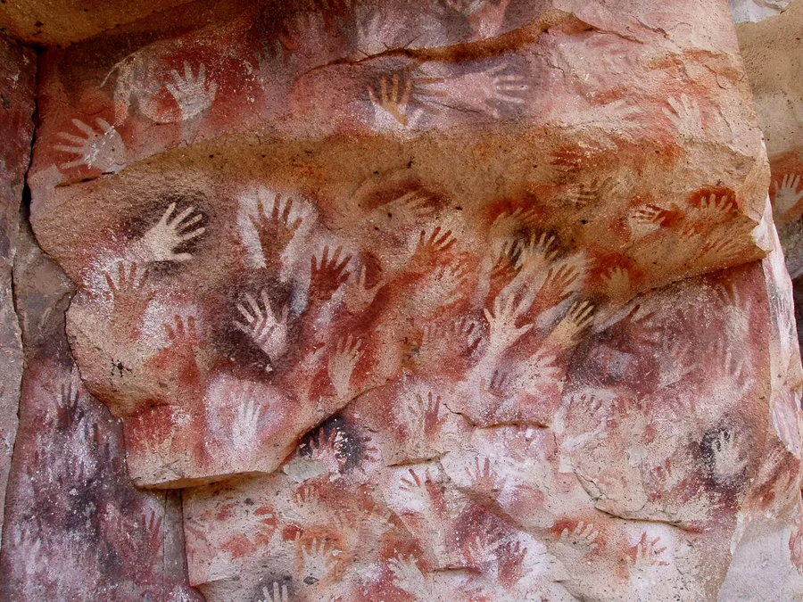 Dozens of stencilled hands in red and ochre across the rock wall of the Cueva de las Manos in Argentina