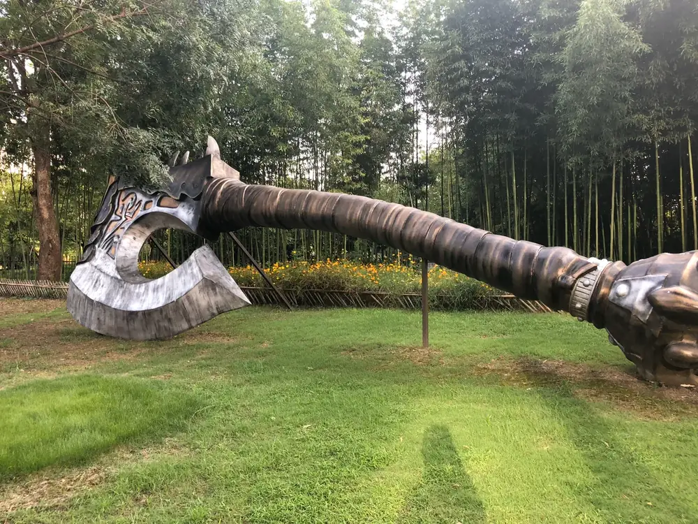 A giant sculpture of a curved orcish axe lying on a lawn among trees