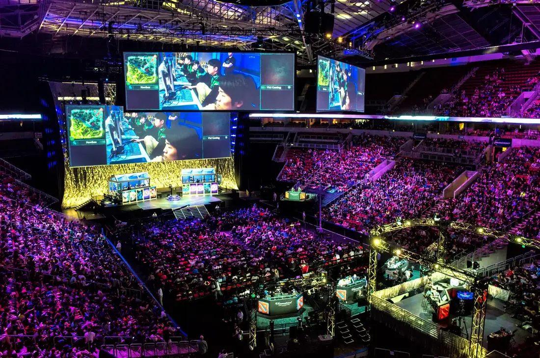 A packed arena lit in purple with a huge screen showing a Dota 2 match