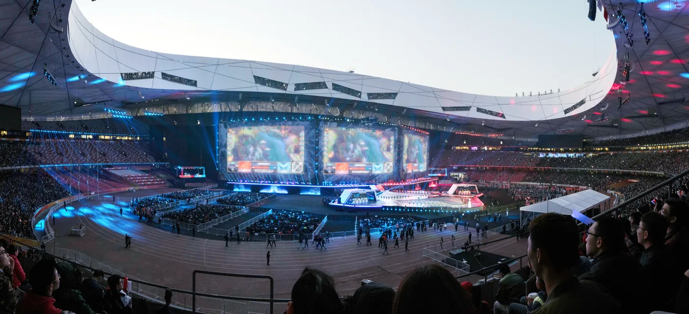 A vast stadium at night, packed, with a lit stage and giant screens at one end