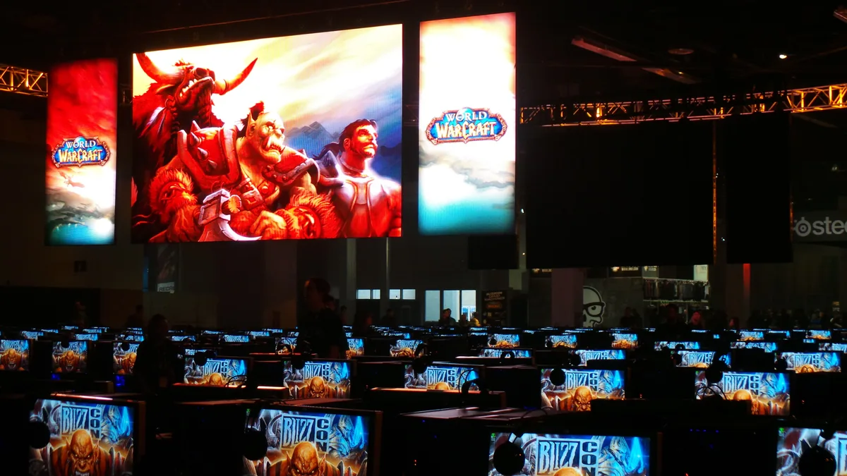 Rows of demo PCs under a large World of Warcraft banner at a convention