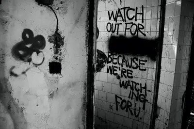 Black and white photograph of graffiti on a tiled hospital wall at Bangour reading 'watch out... because we're watching for u'