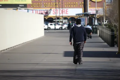 A man walking away down a wide boardwalk past shuttered units and a liquor store sign