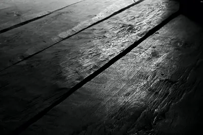 Old wooden floorboards in near darkness, low light catching the grain, black and white