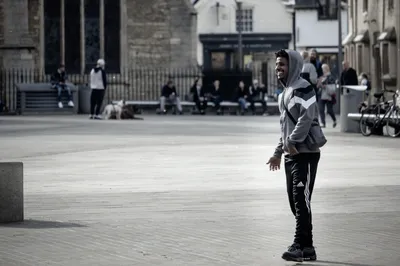 A young man in a grey hooded top crossing an empty paved square, half turned towards the camera