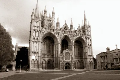 The Gothic west front of Peterborough Cathedral with its three tall arches, a paved square in front, black and white