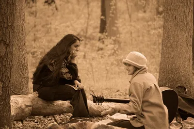 Two people sitting on a log in the woods with a guitar