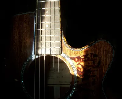 Close-up of an acoustic guitar in low light, sunlight catching the strings, fretboard, and ornate pickguard