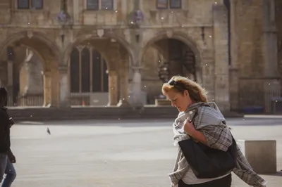 A woman walking briskly across a sunlit historic plaza, bag over one shoulder