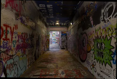 A long covered passage with graffiti on both walls, the floor and the ceiling, daylight at the far end
