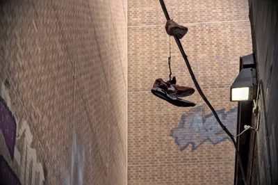 A pair of trainers hanging by their laces from a cable between two graffiti-marked brick walls, a floodlight on one wall