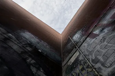 Looking straight up between two tall walls covered in faded grey graffiti, a narrow V of white sky between them