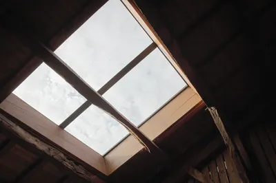 A four-pane skylight in a dark wooden attic roof, bright sky showing through