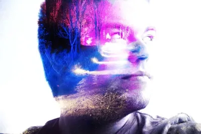 A double-exposure portrait of a face blended with a landscape of trees and light